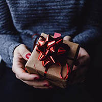 holding out a small wrapped gift with a red ribbon and bow