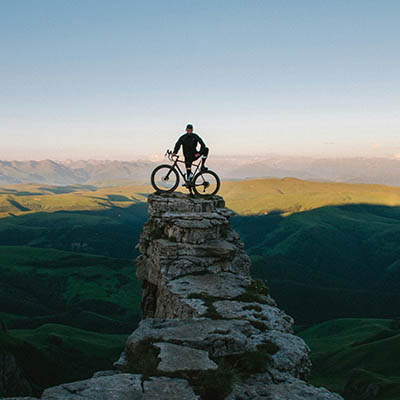 man on a cycle at the top of a mountain with a sunny view in the background